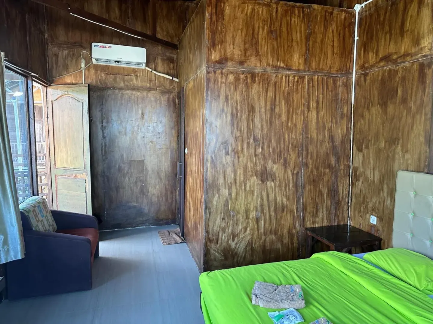 Room interior at Mooi Park in Sorong with bed, seating area, air conditioner, and wooden walls.
