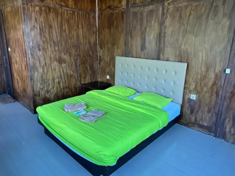 Standard room at Mooi Park in Sorong with a bright green bedspread, upholstered headboard, and wood-paneled walls.