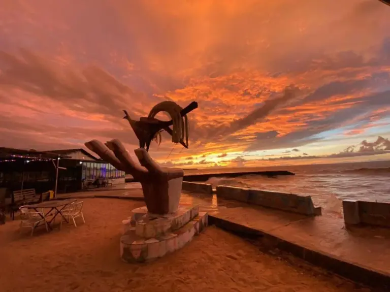 Sunset beach view at Mooi Park in Sorong with dramatic orange sky, seaside sculpture, and ocean horizon.