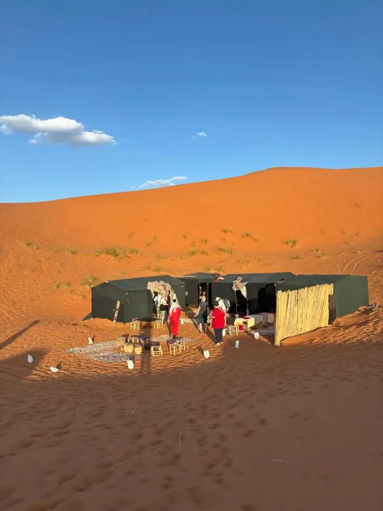 Moroccan Desert Camp in Merzouga tented camp exterior surrounded by orange sand dunes in the desert