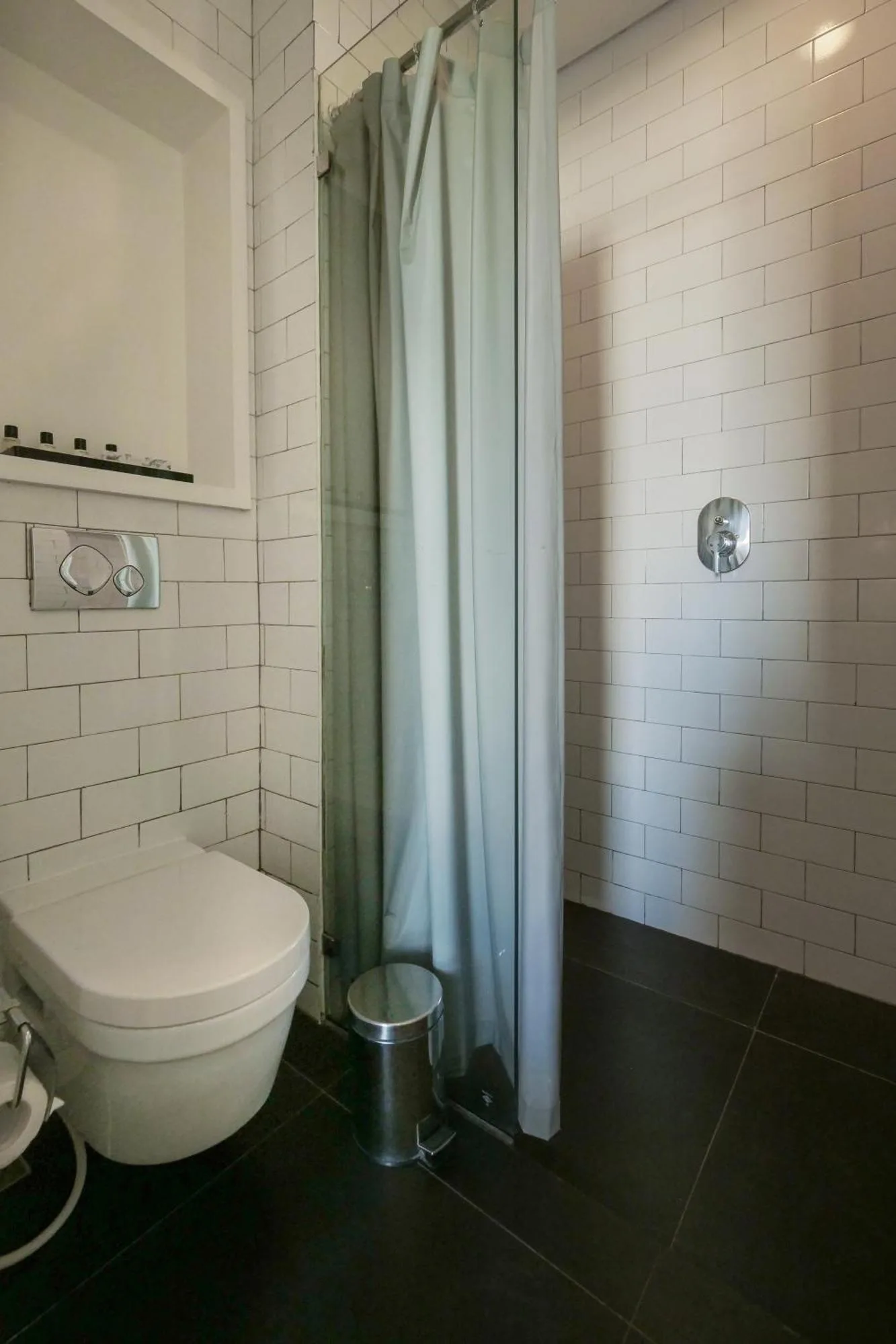 Badezimmer im Morrissey Hotel Jakarta mit Dusche, Toilette und weißen Fliesenwänden.