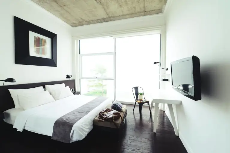 Helles Schlafzimmer im Morrissey Hotel Jakarta mit Queensize-Bett, dunklem Holzboden und großem Fenster.