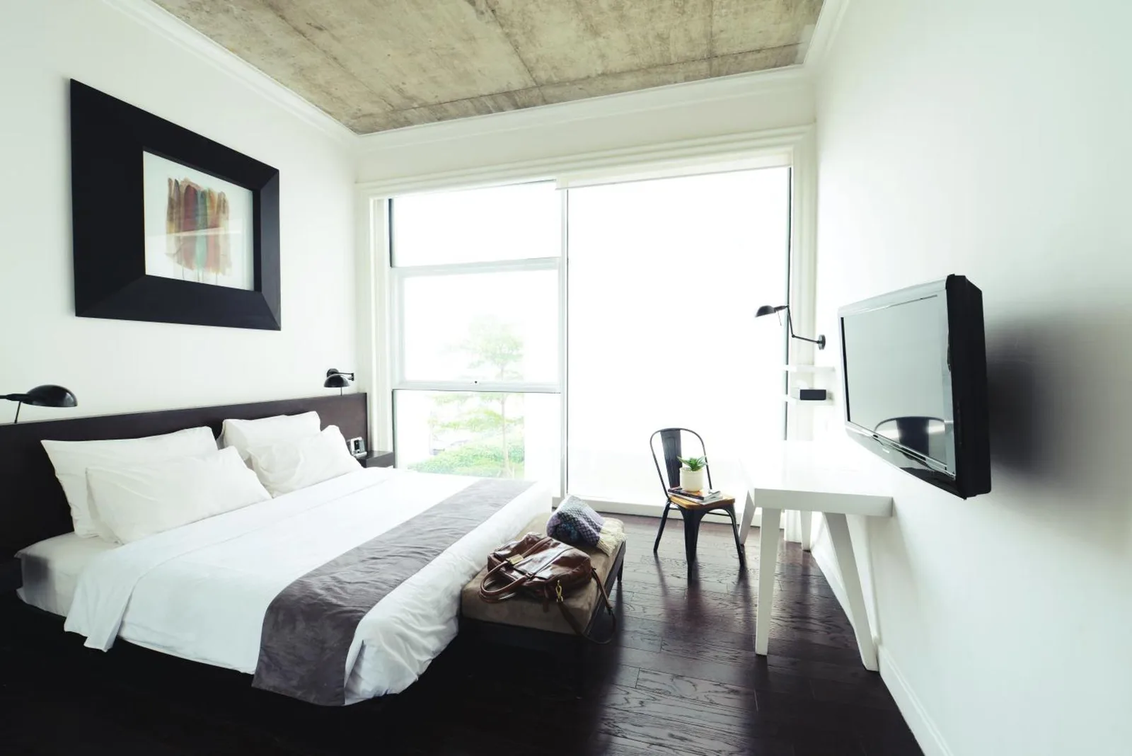 Helles Schlafzimmer im Morrissey Hotel Jakarta mit Queensize-Bett, dunklem Holzboden und großem Fenster.