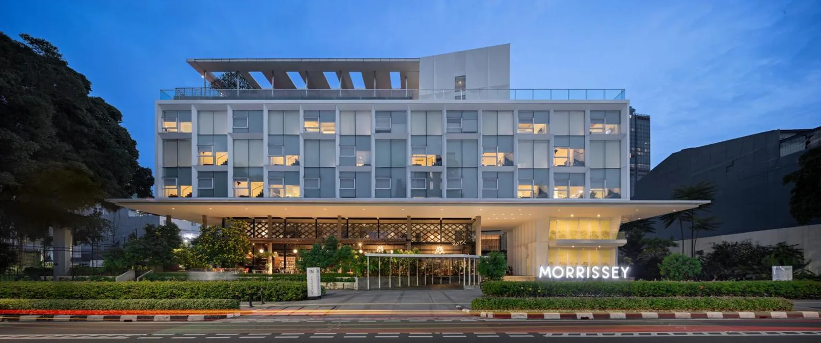 Außenansicht des Morrissey Hotel in Jakarta mit moderner Fassade in der Abenddämmerung.