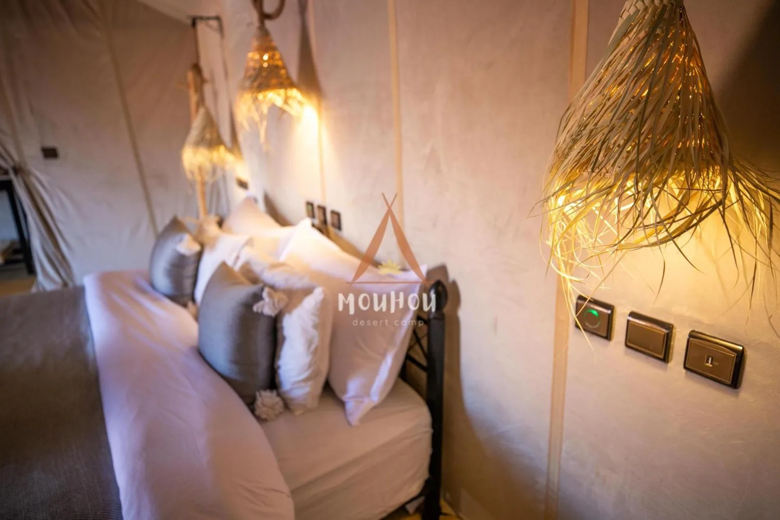 Primer plano de la cama y las luces de pared dentro de Mouhou Desert Camp en Merzouga