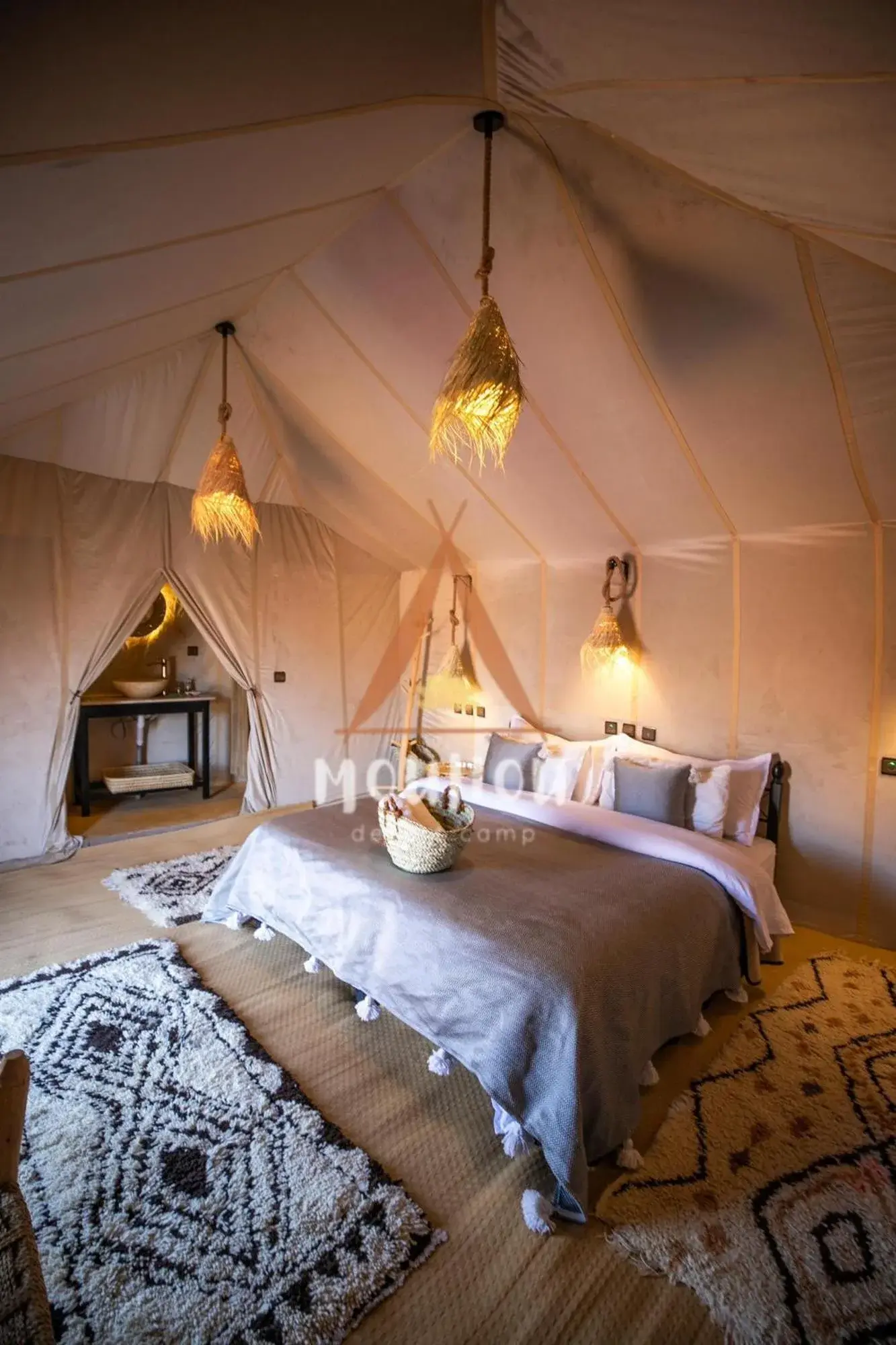 Amplio dormitorio de tienda en Mouhou Desert Camp en Merzouga con luces tejidas y alfombras estampadas