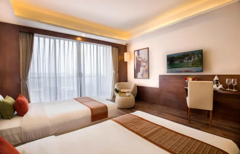 Chambre double au Mountain Glory Forest Resort and Spa, Pokhara avec deux lits, un espace de travail et des portes-fenêtres donnant sur le balcon.