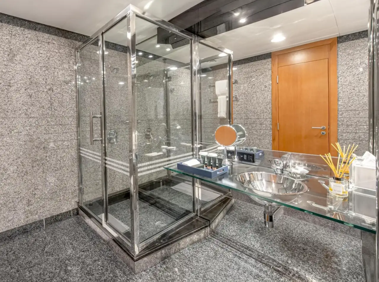 Salle de bains élégante au Mövenpick Dubai Creek à Dubai avec cabine de douche vitrée, lavabo et articles de toilette.