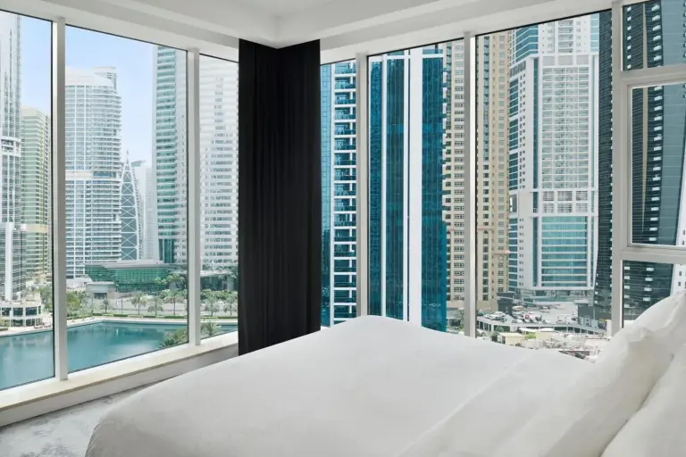 Dormitorio en Mövenpick Hotel Jumeirah Lakes Towers Dubai con cama junto a ventanales y vistas al skyline de Dubai