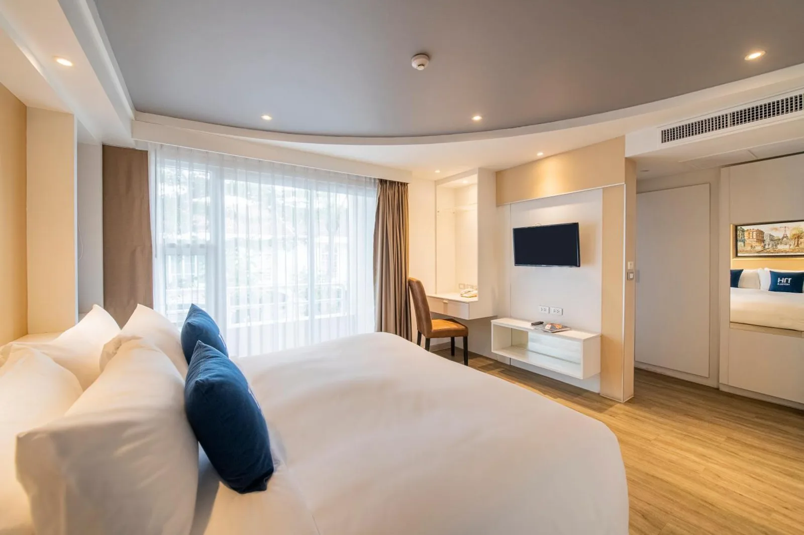 Side angle of a guest bedroom at NH Boat Lagoon Phuket Resort in Phuket with seating and large window.