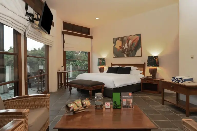 Suite au Novus Giri Resort & Spa à Sukabumi avec un lit king-size, un coin salon et de grandes fenêtres.
