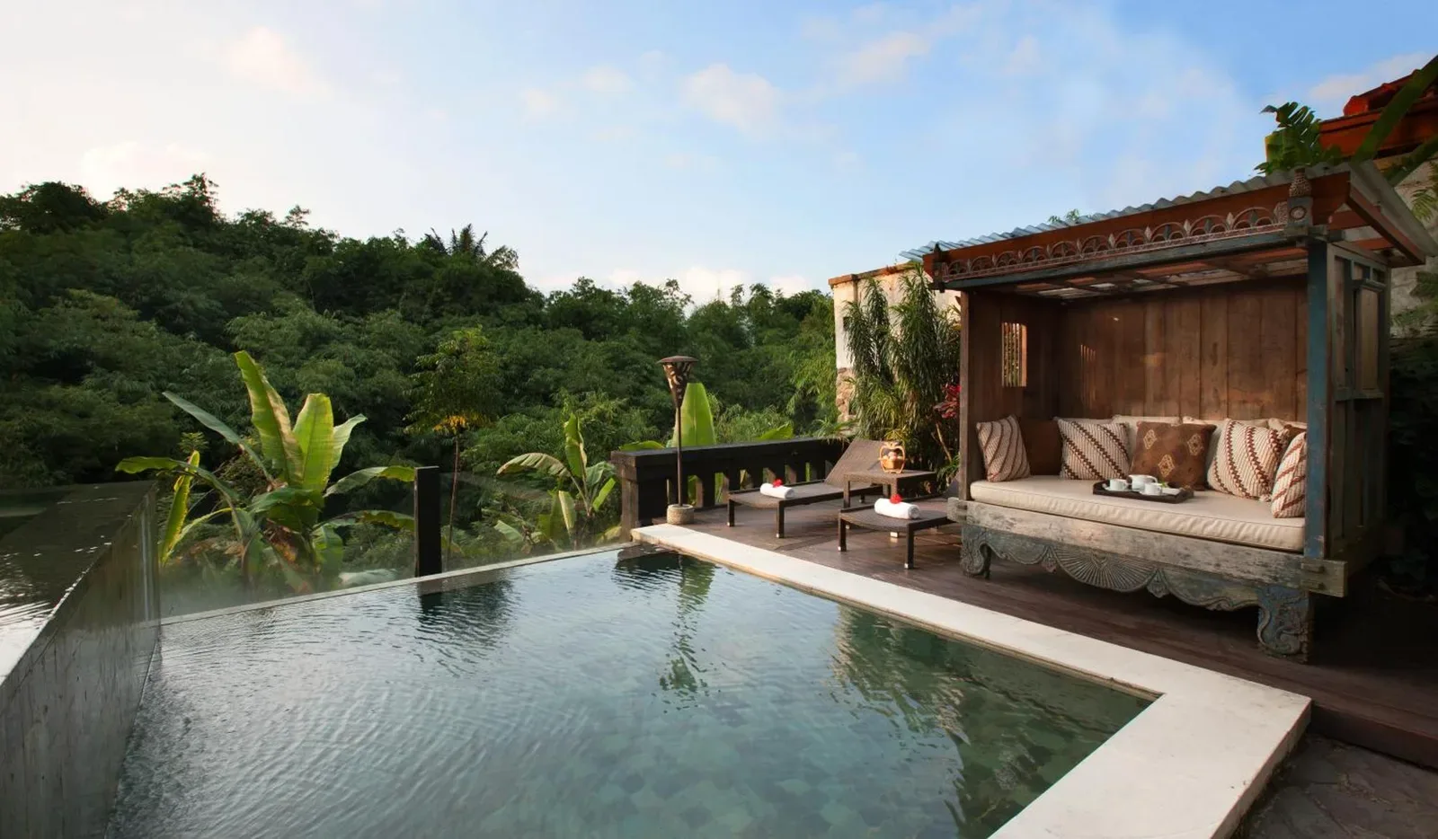 Piscine privée de villa au Novus Giri Resort & Spa à Sukabumi avec un lit de repos en bois et une vue sur le jardin tropical.