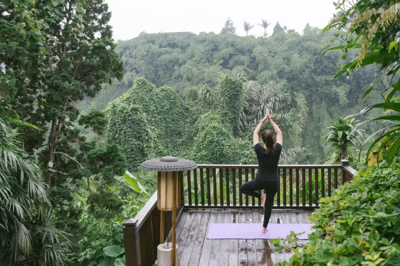Plateforme de yoga au Novus Giri Resort & Spa à Sukabumi avec un client pratiquant le yoga au-dessus d’une vallée boisée.