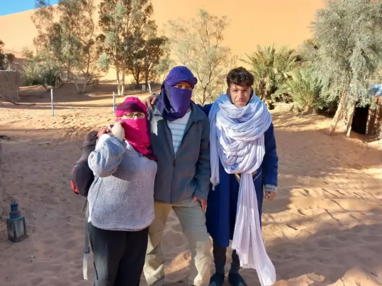 Oasis Desert Camp Obira à Merzouga avec trois clients debout ensemble en tenue désertique dans le camp