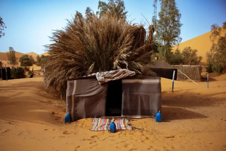 Oasis Desert Camp Obira à Merzouga montrant une petite tente traditionnelle dans le désert avec un tapis tissé et des dunes à proximité