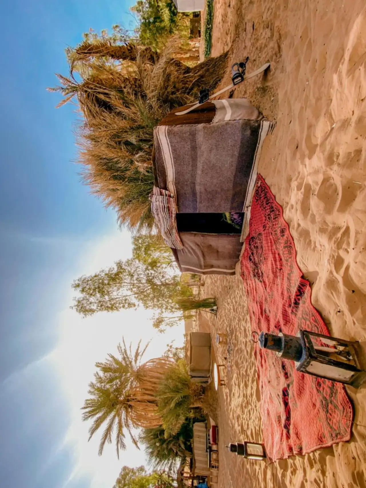 Oasis Desert Camp Obira à Merzouga avec une tente désertique entourée de sable, de tapis et de palmiers
