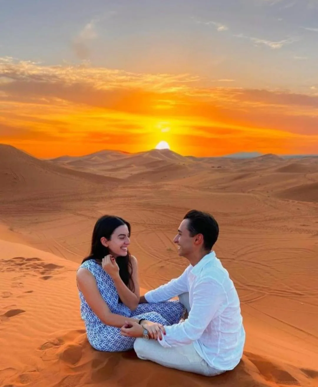 Un couple assis sur les dunes au coucher du soleil près de Overnight Desert Camp à Merzouga.