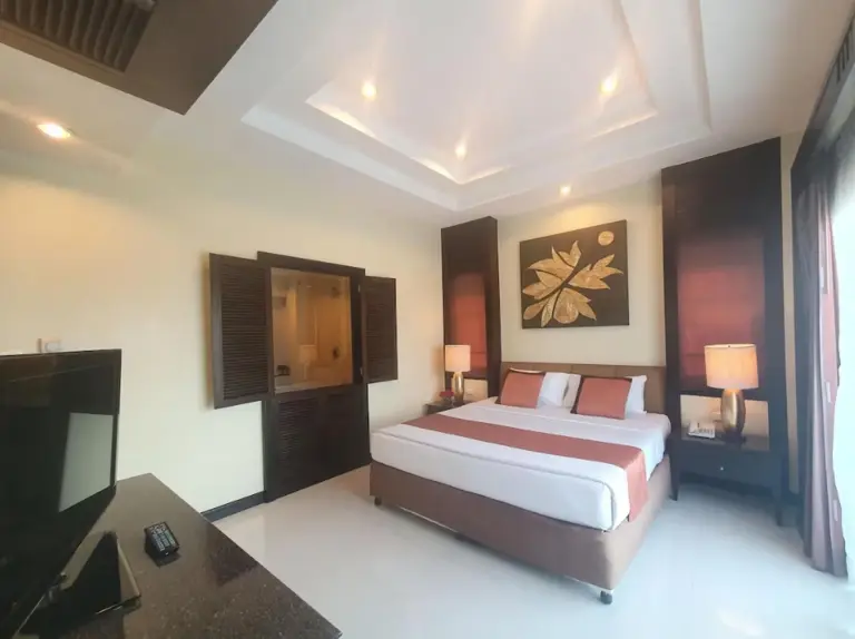Interior del dormitorio en Palette Luxe North Pattaya en Pattaya con cama king, TV y cálidos detalles en madera