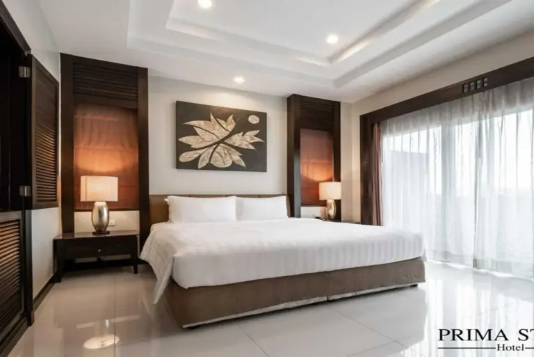 Elegante dormitorio king en Palette Luxe North Pattaya en Pattaya con ropa de cama blanca, detalles en madera y grandes ventanales