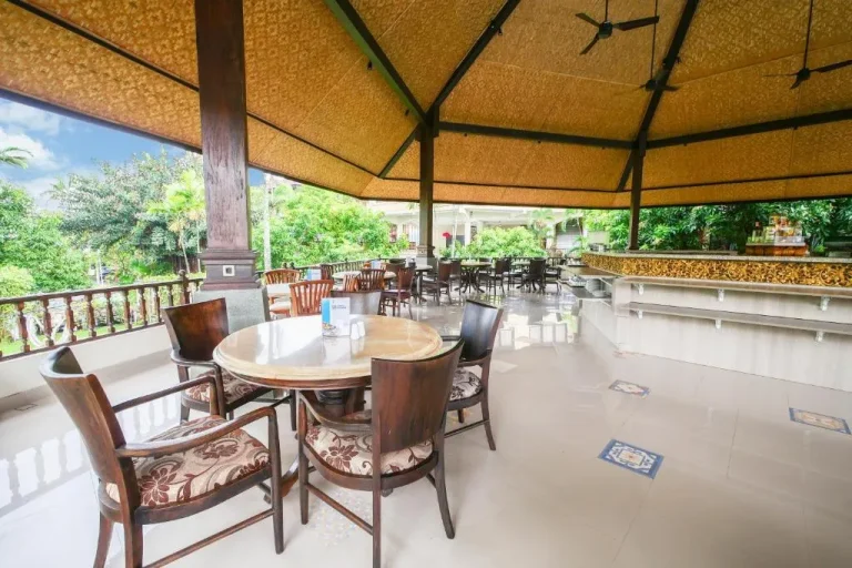 Área de comedor en Palm Beach Hotel Bali con mesas de madera y una vista tropical.