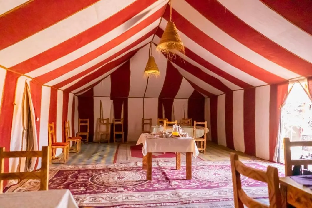 Restaurant tent interior at Planet Sahara Camp in Merzouga with striped fabric and tables
