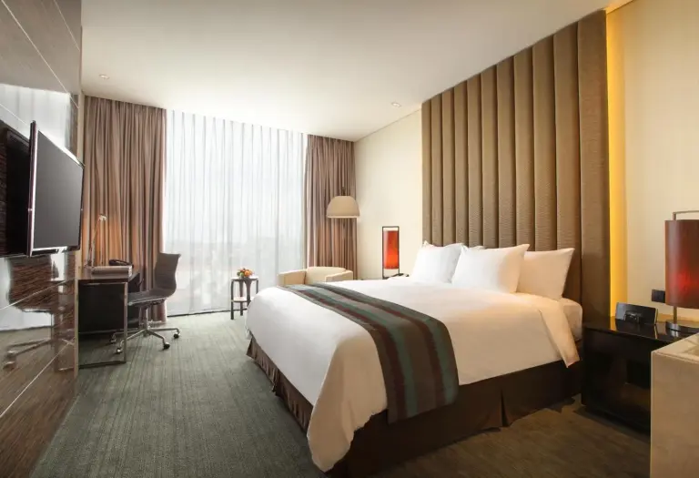 Cómoda habitación deluxe en PO Hotel Semarang en Semarang con cama king, escritorio de trabajo y ventana de suelo a techo.