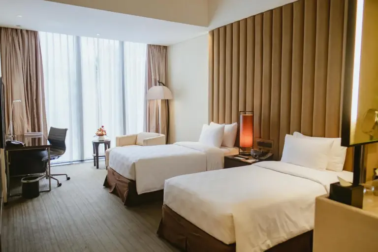 Habitación doble de huéspedes en PO Hotel Semarang en Semarang con dos camas, sillón y cortinas de suelo a techo.