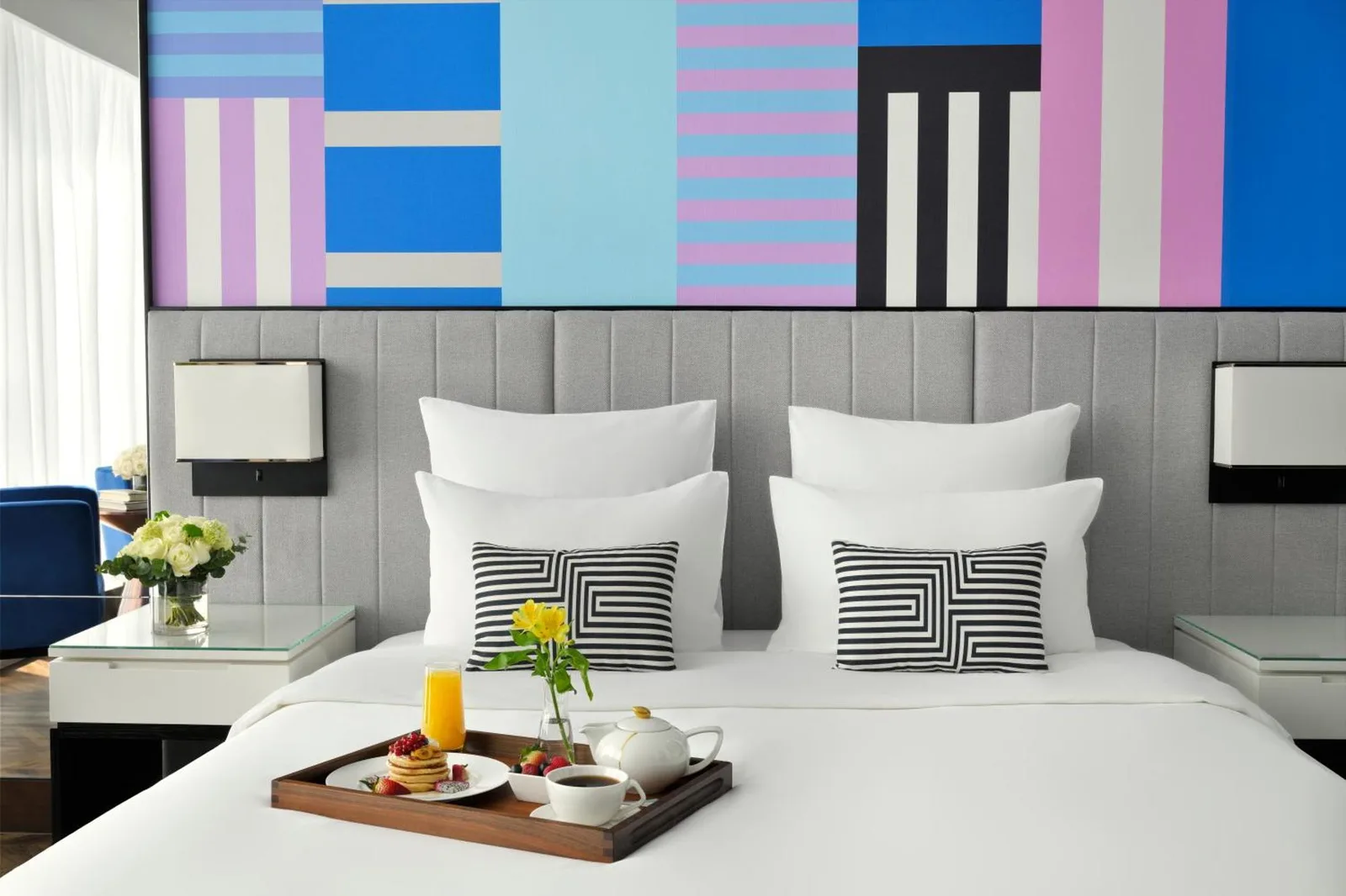 Vista de la cama en Pullman Dubai Downtown en Dubai con arte mural colorido y bandeja de desayuno
