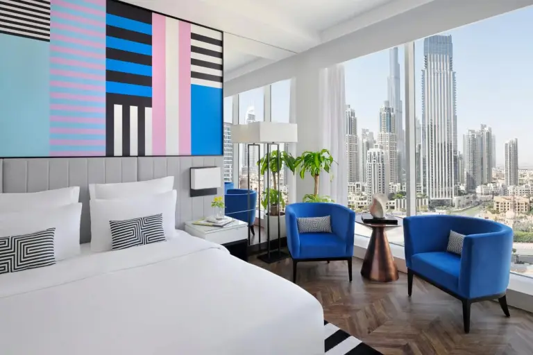 Suite de esquina en Pullman Dubai Downtown en Dubai con cama, sillas azules y panorama del skyline