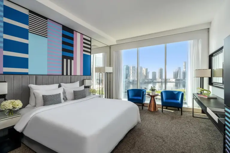 Dormitorio de suite en Pullman Dubai Downtown en Dubai con ventanas con vistas a la ciudad y sillas azules de descanso