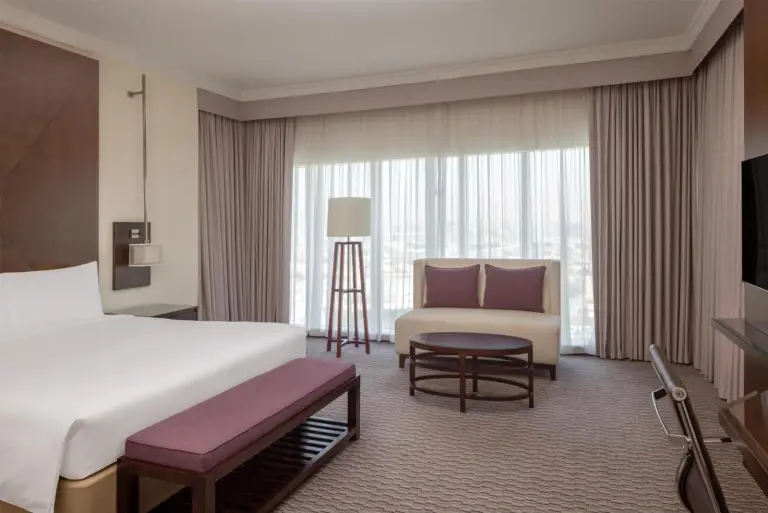 Chambre de type suite au Radisson Blu Hotel, Dubai Barsha Heights avec lit king, canapé, table basse et grandes fenêtres.