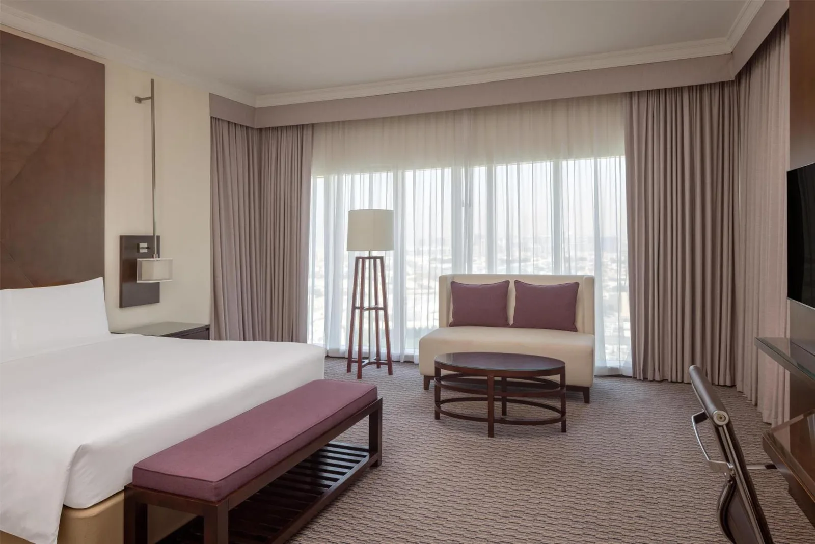 Chambre de type suite au Radisson Blu Hotel, Dubai Barsha Heights avec lit king, canapé, table basse et grandes fenêtres.