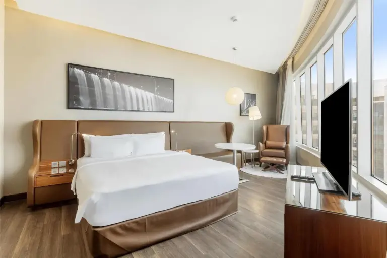 King bedroom at Radisson Blu Hotel, Dubai Canal View with a bed, lounge chair, and city-facing windows