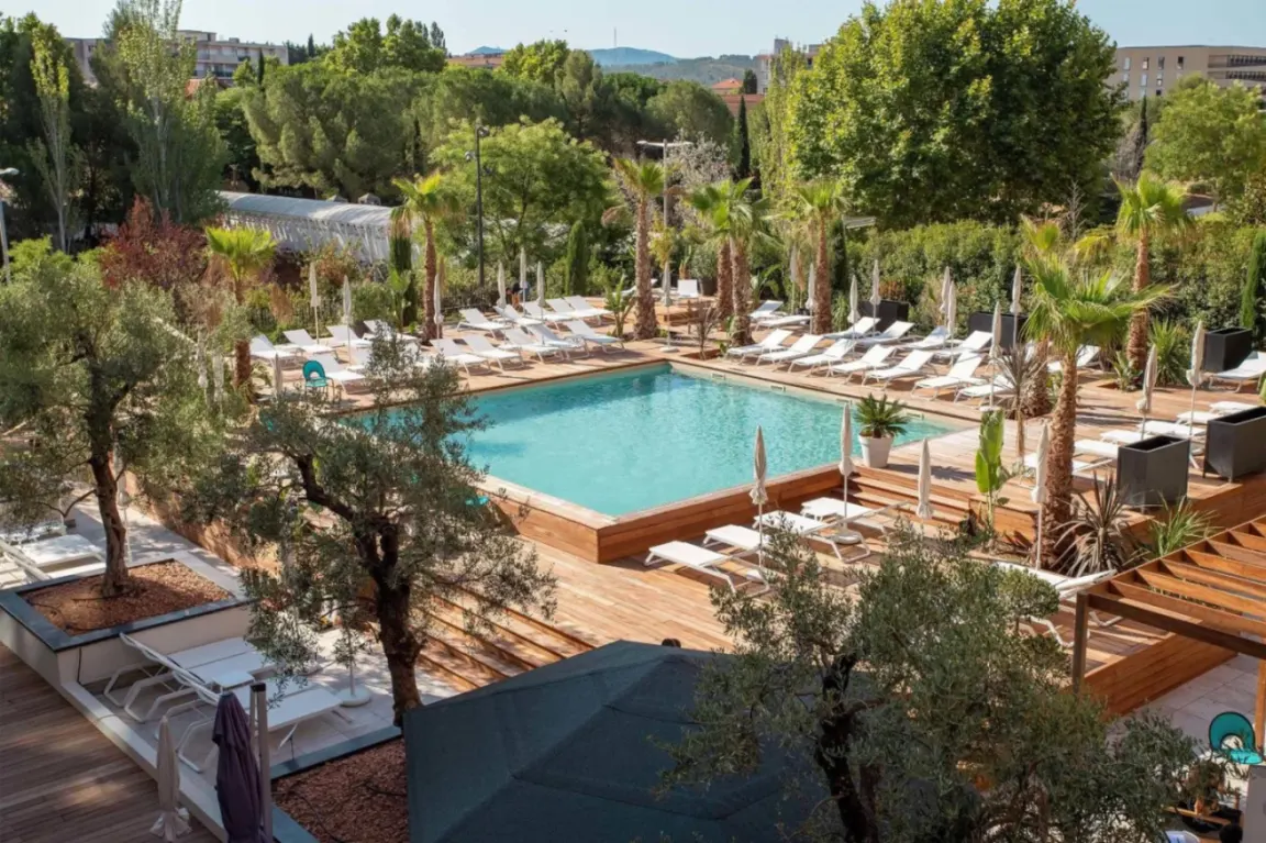 Zona de la piscina del Renaissance Aix-en-Provence Hotel con tumbonas y palmeras