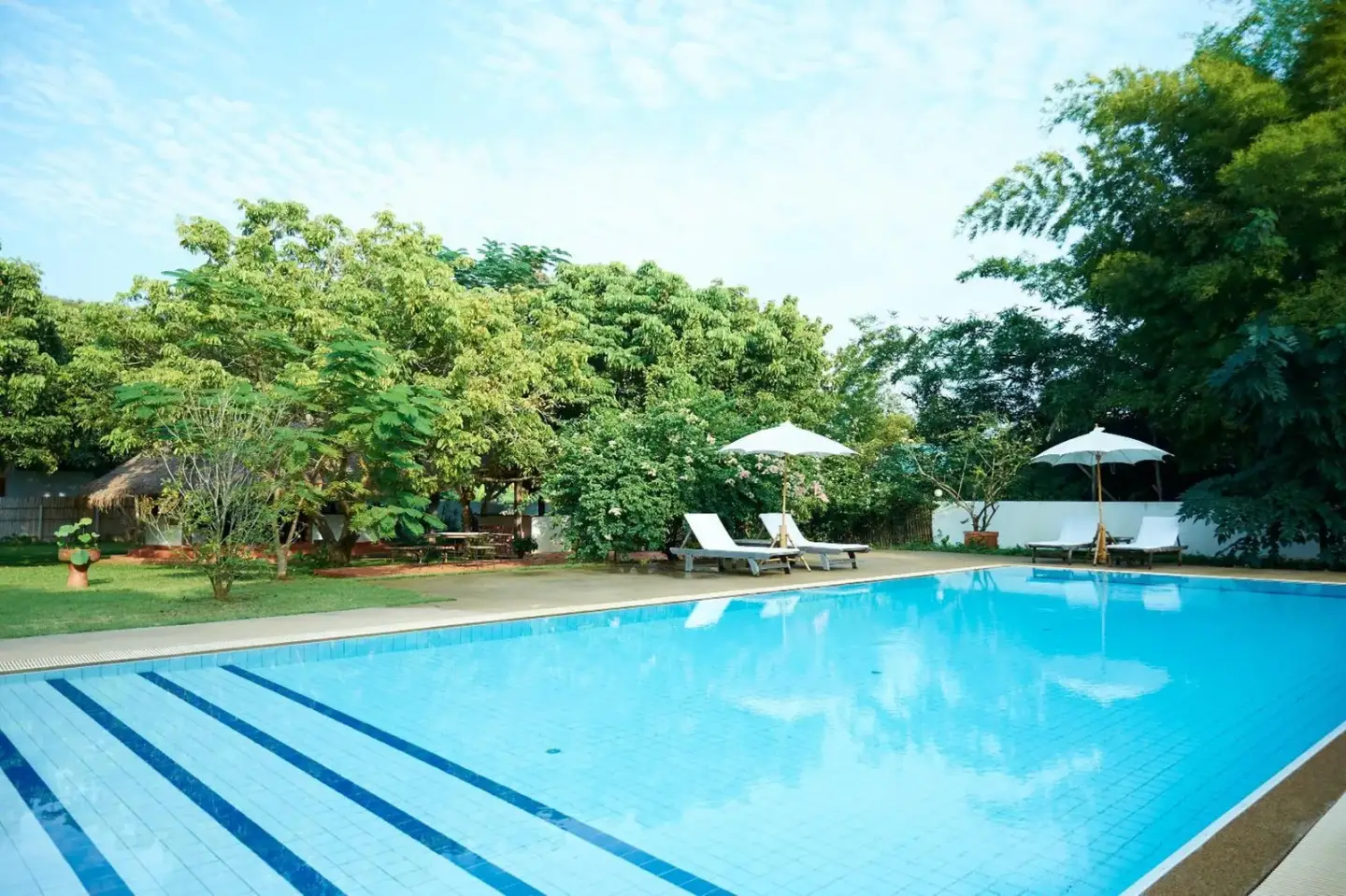 Piscina al aire libre de Resort Hoshihana Chiang Mai rodeada de árboles tropicales y tumbonas