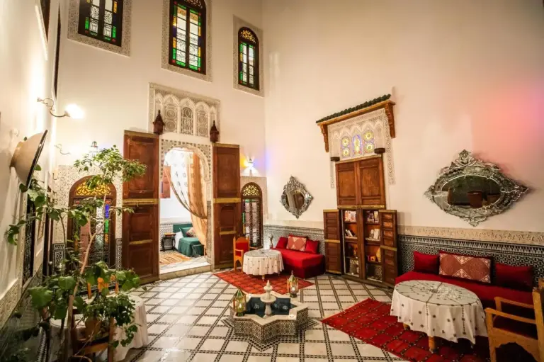 Elegant courtyard at Riad Arabella in Fes with arched doors, stained glass, red seating, and mosaic floors.