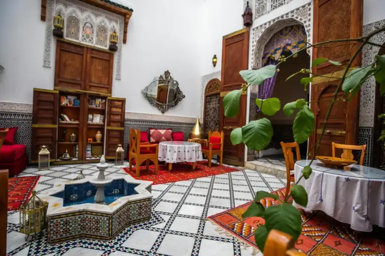 Courtyard seating area at Riad Arabella in Fes with plants, mosaic fountain, and traditional decorative architecture.