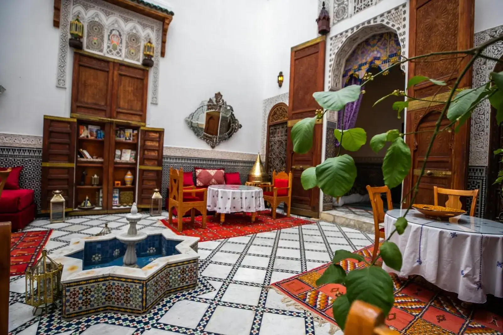 Courtyard seating area at Riad Arabella in Fes with plants, mosaic fountain, and traditional decorative architecture.