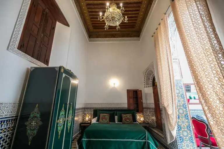 Bright guest room at Riad Arabella in Fes with traditional Moroccan decor, a green bed, and carved details.