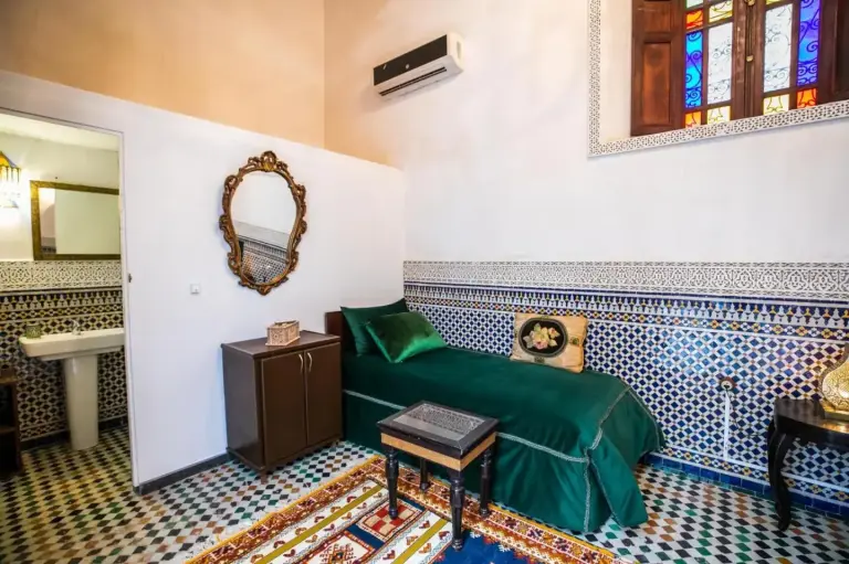 Single room at Riad Arabella in Fes with a green bed, patterned tile walls, and a small bathroom entrance.