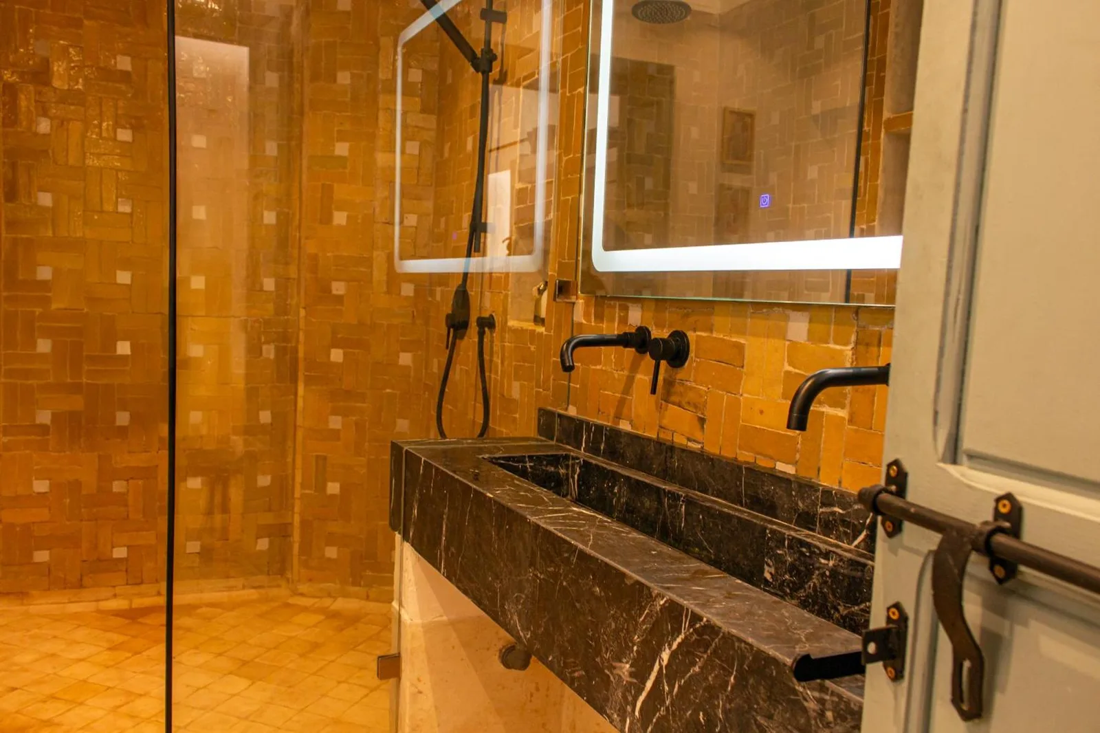 Riad Dar Ben Slimane in Marrakesch Badezimmer mit Mosaikfliesenwänden, einem schwarzen Steinwaschbecken und Glasdusche