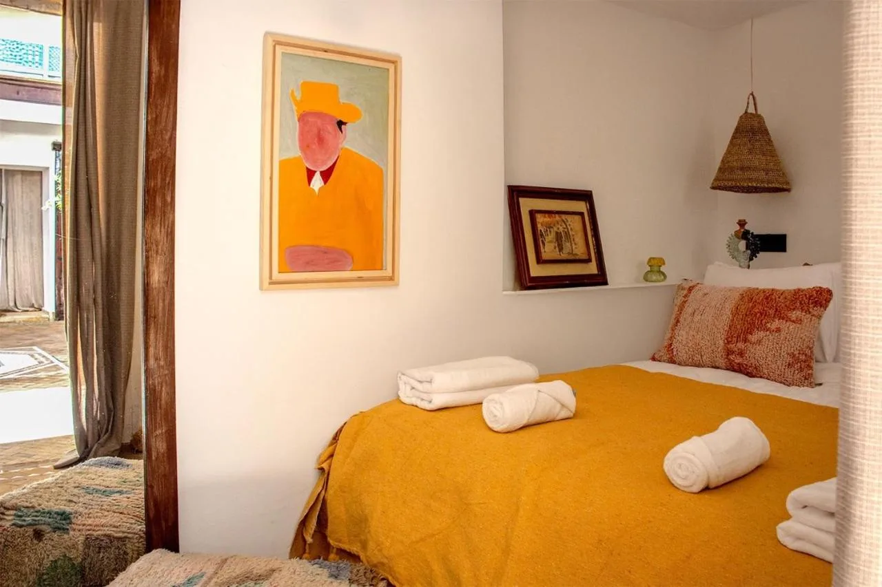 Riad Dar Ben Slimane in Marrakesch Schlafzimmer mit gelber Tagesdecke, Handtuchrollen, Wandkunst und geflochtenen Lampen