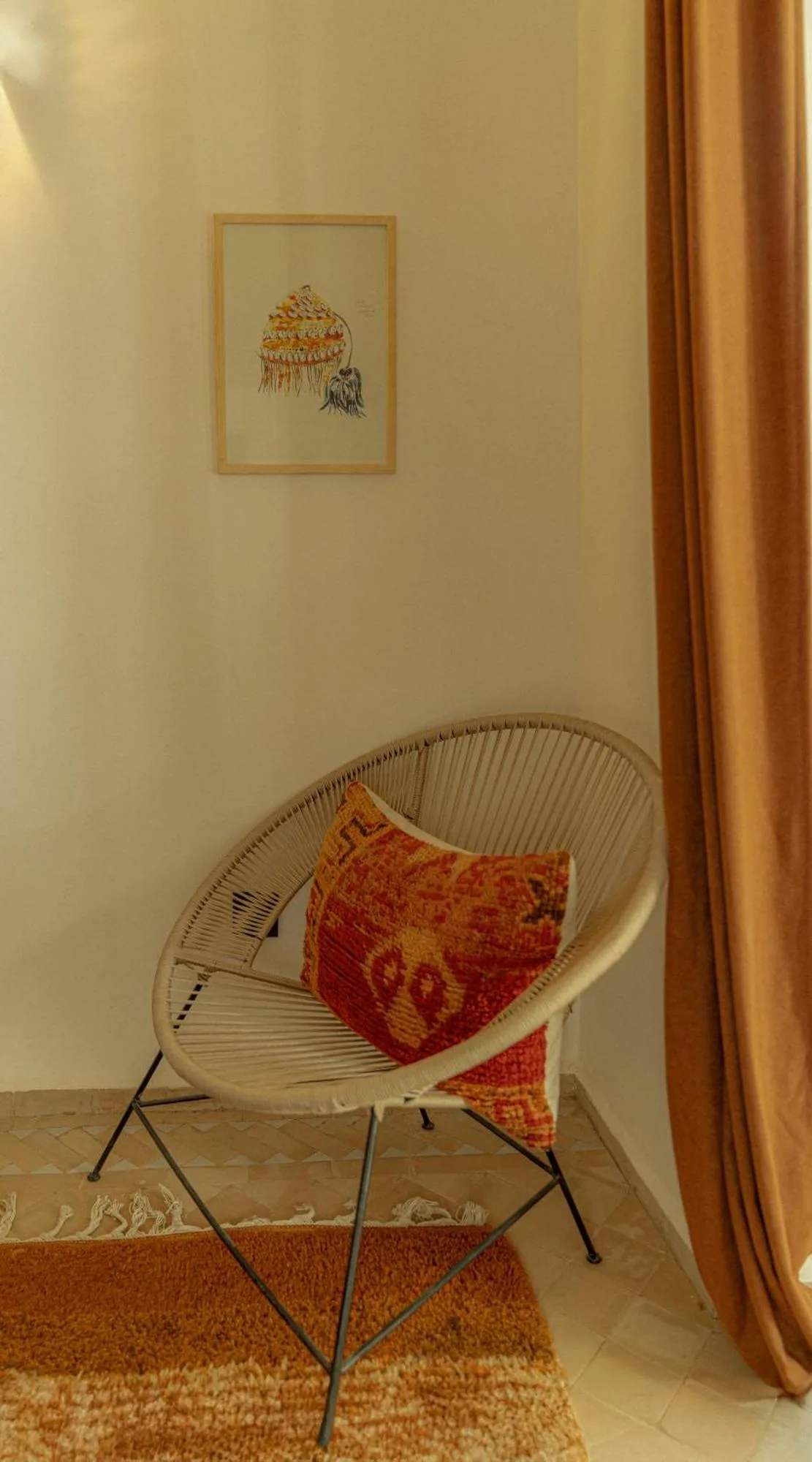 Riad Dar Ben Slimane in Marrakesch Leseecke mit einem Rattanstuhl, gemustertem Kissen, Vorhang und Wandkunst