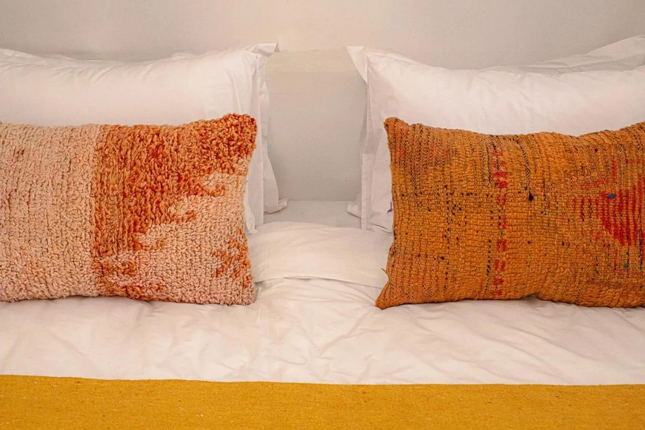 Riad Dar Ben Slimane in Marrakesch Suite-Bett mit weißer Bettwäsche und strukturierten orangefarbenen Kissen