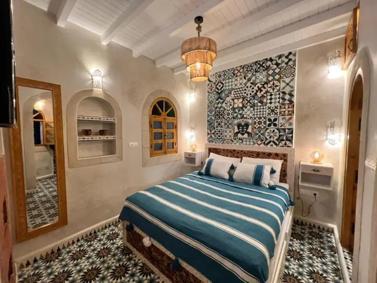 Dormitorio de huéspedes en Riad dar el hania en Essaouira con cama verde azulado, baldosas estampadas y pequeños nichos empotrados
