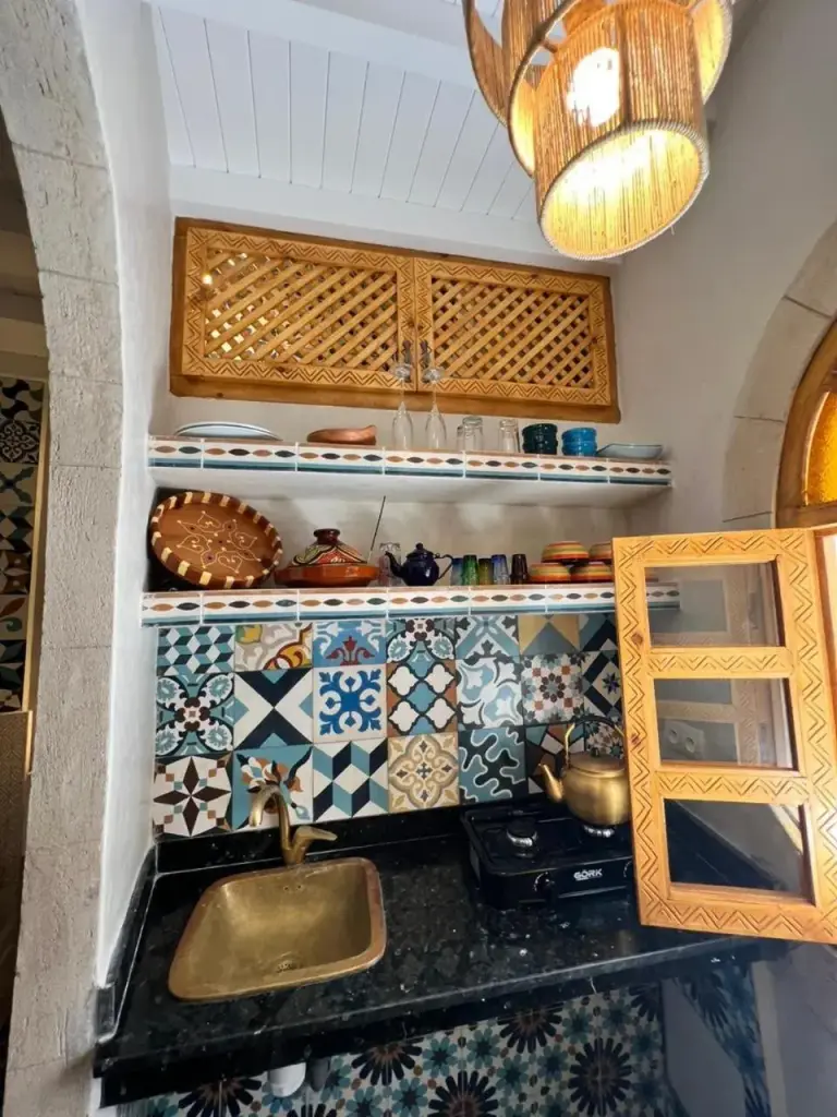 Estantes de cocina abiertos en Riad dar el hania en Essaouira con cerámica, vasos y baldosas decorativas marroquíes