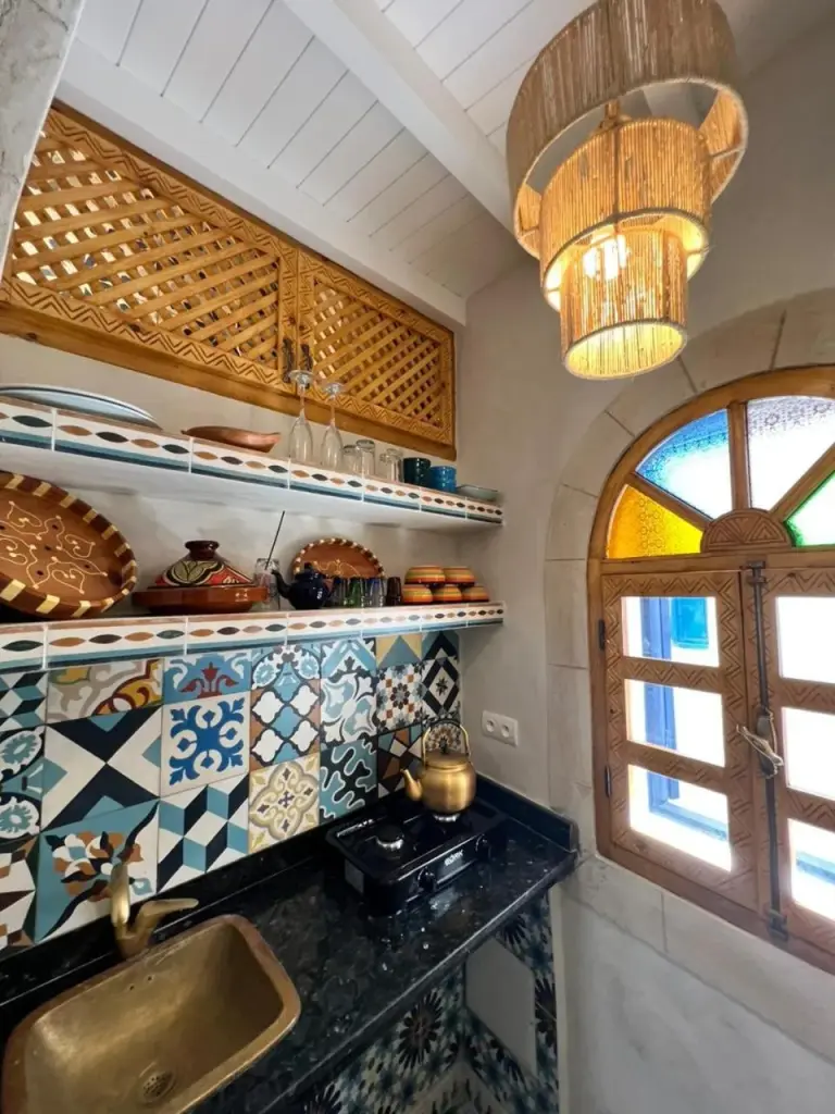Rincón tradicional de kitchenette en Riad dar el hania en Essaouira con fregadero de latón, estantes y ventana arqueada