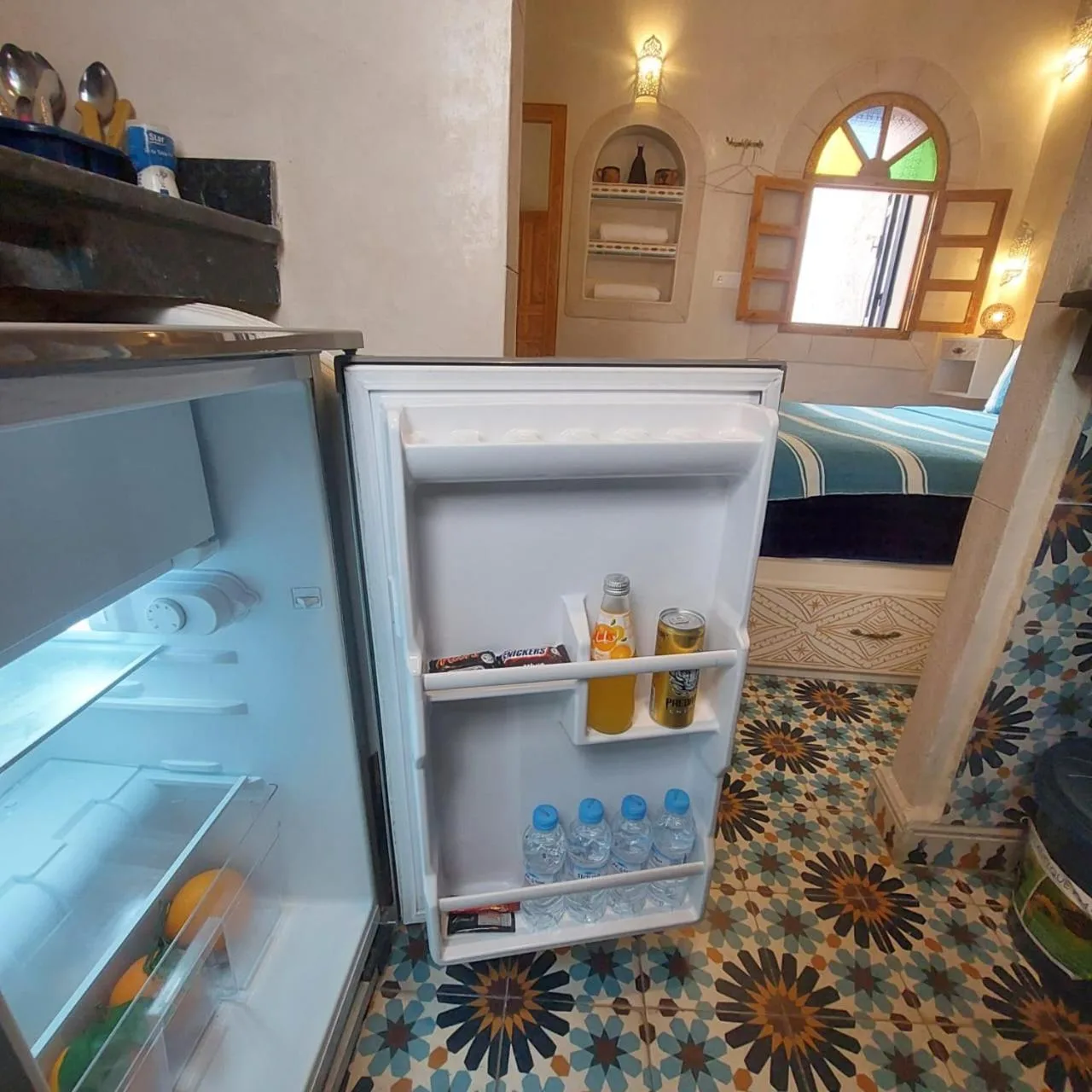 Mini nevera abierta y zona de dormitorio en Riad dar el hania en Essaouira con bebidas y suelo estampado