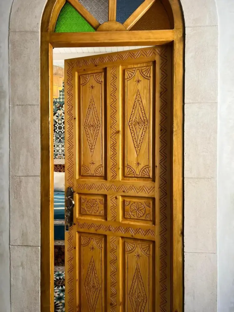 Puerta de madera tallada en Riad dar el hania en Essaouira con marco arqueado y vidrieras