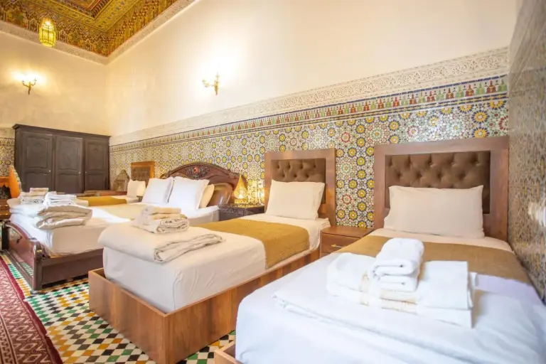 Dormitorio triple en Riad Fes iline Medina en Fes con tres camas individuales, paredes de mosaico marroquí y decoración tradicional en el techo